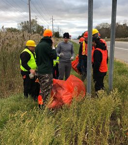Image of people gather on the side of the road putting garbage in a plastic bag.